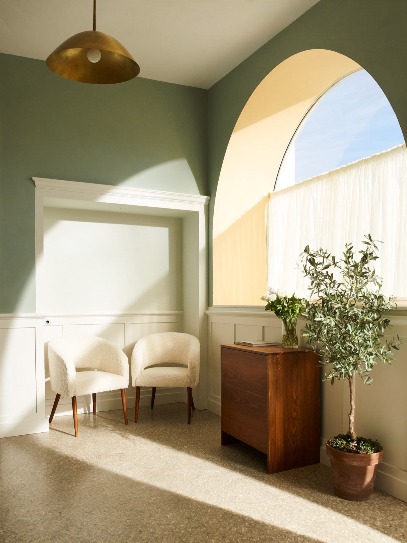 Sunlit reception of the Aster Health office: sage-green walls, oak wainscoting, and a vase of white asters on a walnut desk